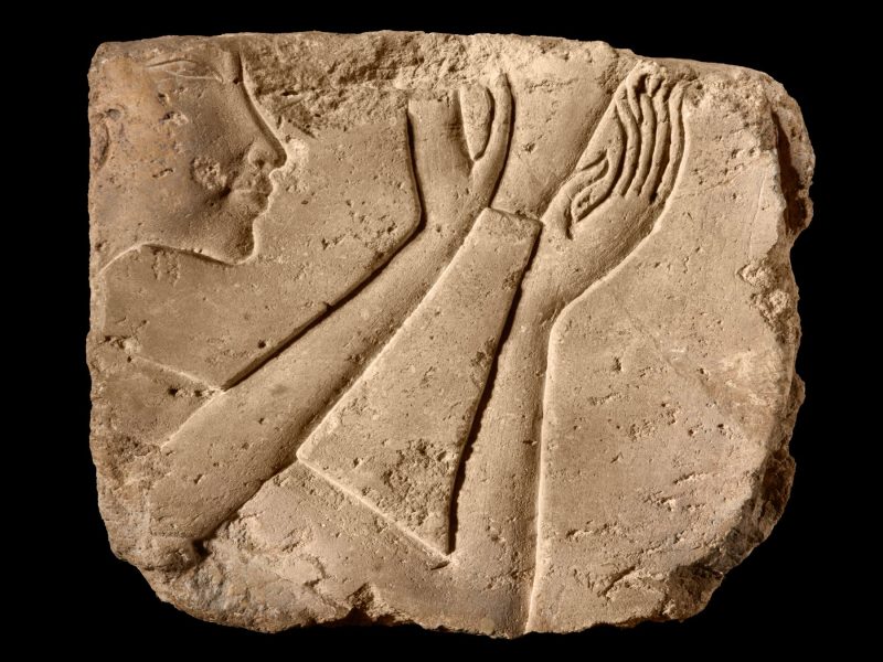 Limestone relief fragment depicting a face and hands in ancient Egyptian style, showcasing craftsmanship from antiquity.