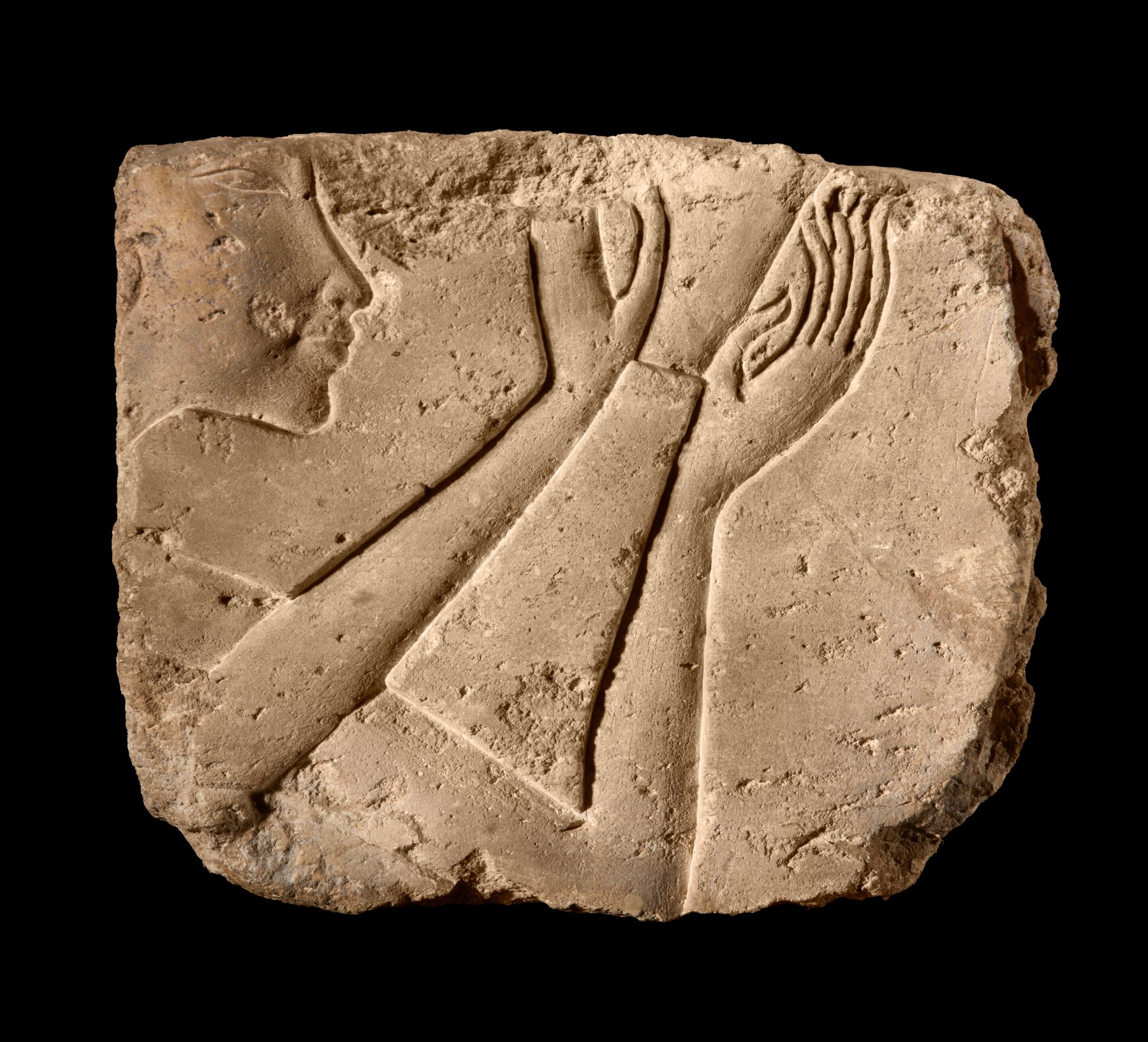 Limestone relief fragment depicting a face and hands in ancient Egyptian style, showcasing craftsmanship from antiquity.