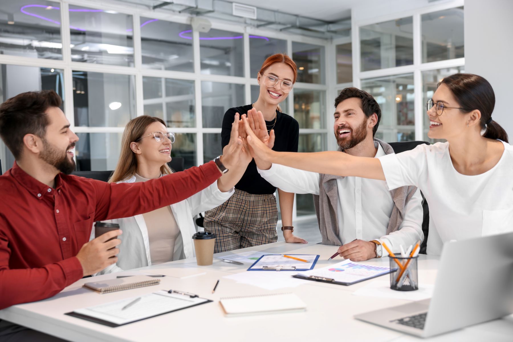 Team members celebrate collaboration with high-fives during a meeting in a modern office setting.