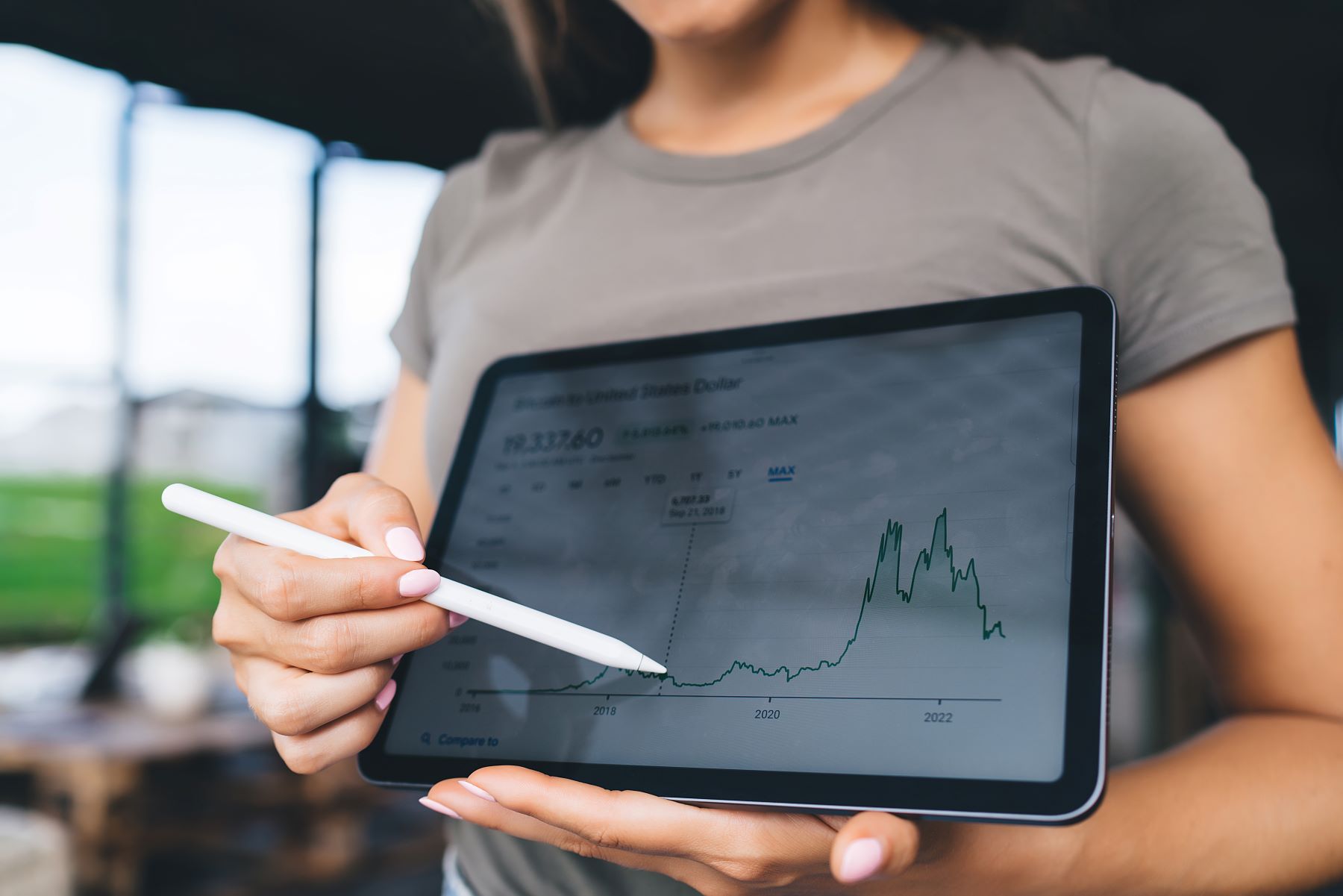 Woman analyzing a cryptocurrency price chart on a tablet, highlighting investment trends and fluctuations over time.