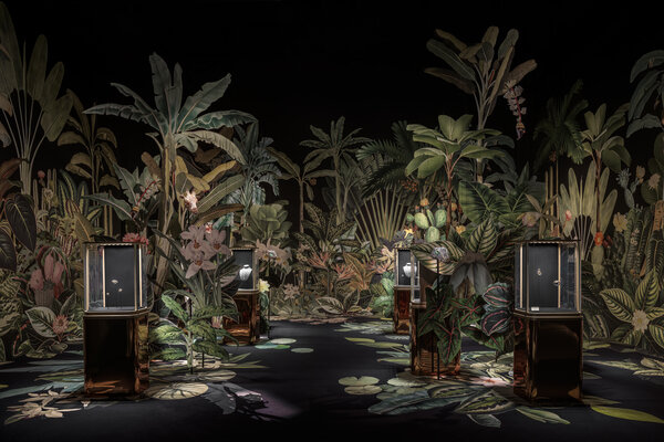 A vibrant exhibition space filled with lush tropical plants and elegant display cases showcasing luxury jewelry.
