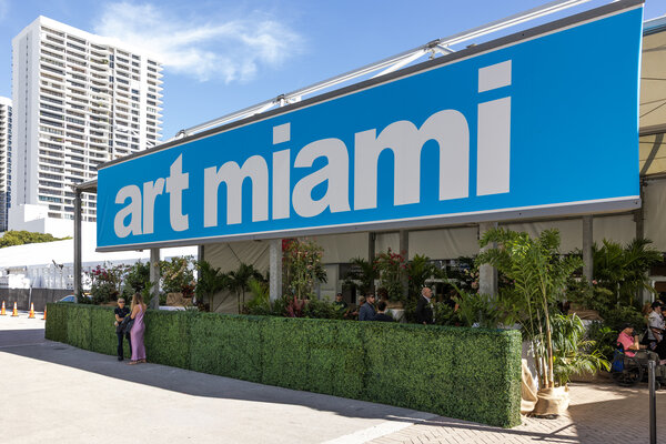Large blue sign displaying "art miami" outside a bustling entrance with greenery and visitors during Art Basel Miami Beach 2025.