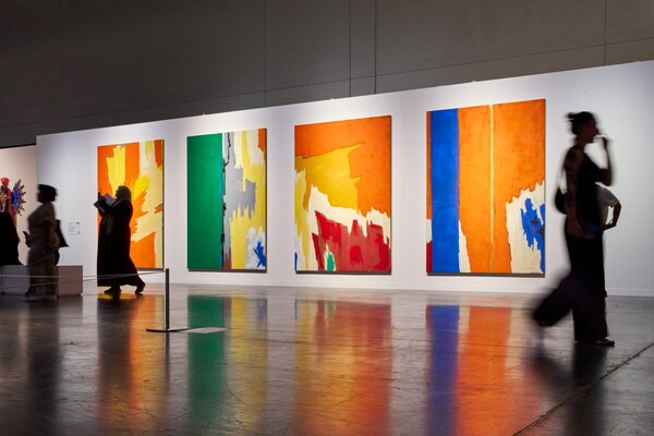 Colorful abstract paintings displayed on white walls, with visitors walking through the art exhibit at Art Basel Miami Beach.