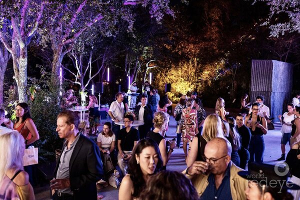 A lively gathering at Art Basel Miami Beach 2025, showcasing diverse attendees enjoying the festive atmosphere amidst vibrant lighting.