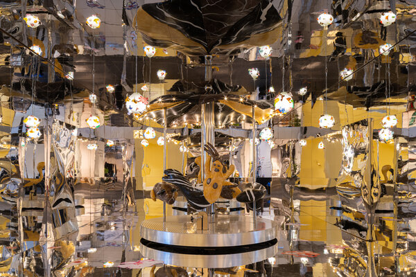 A reflective art installation with whimsical light fixtures and an abstract centerpiece at Design Miami 2025.