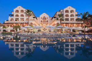 Hacienda del Mar's stunning architecture reflects in the serene pool, surrounded by umbrellas and palm trees at twilight.