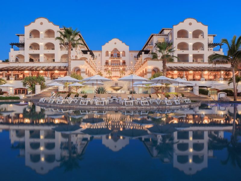 Hacienda del Mar's stunning architecture reflects in the serene pool, surrounded by umbrellas and palm trees at twilight.
