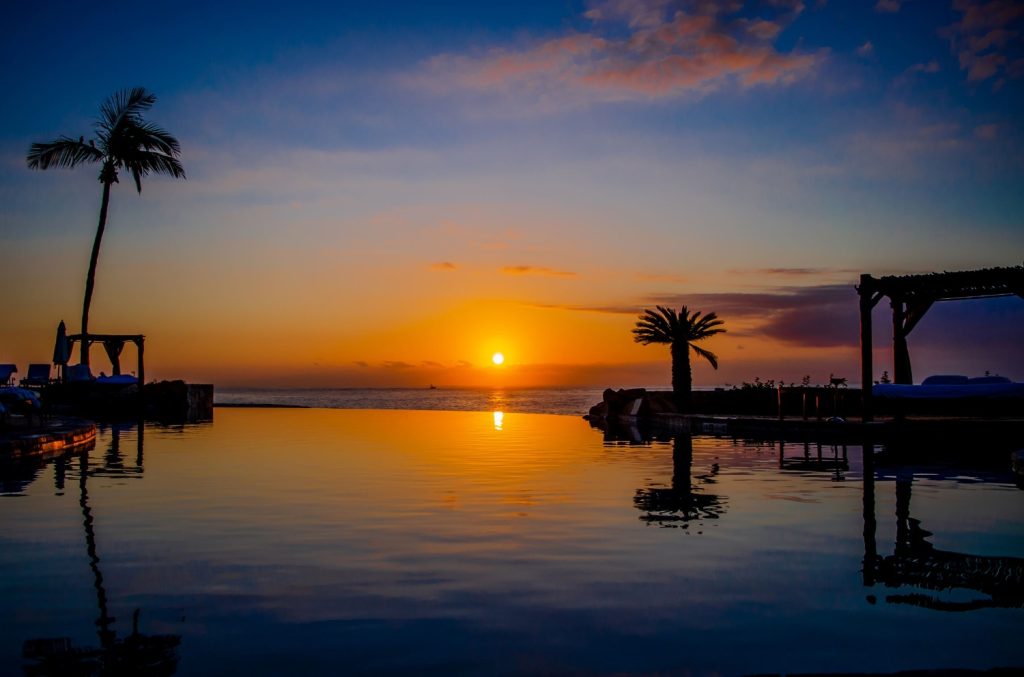 Sunset over a tranquil pool with palm trees, reflecting vibrant colors of the sky at Hacienda del Mar.