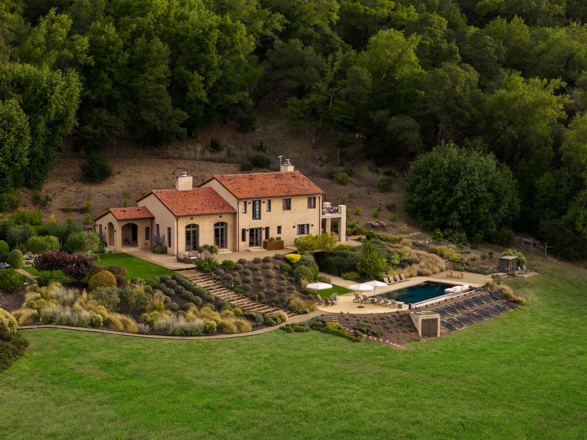 Luxury home with a terracotta roof, beautifully landscaped gardens, and a swimming pool set in a serene natural environment.