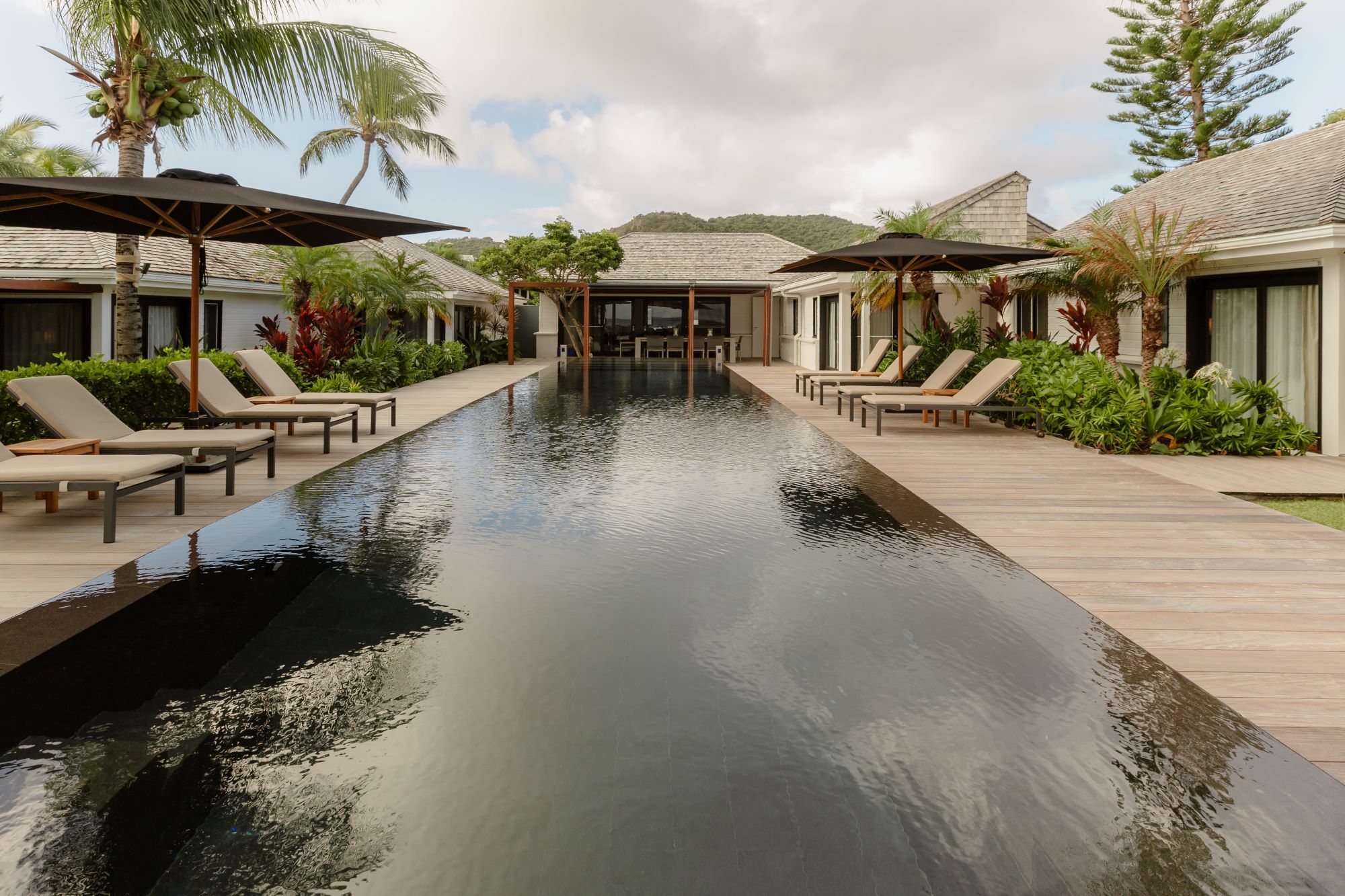 Luxurious villa with infinity pool, lounge chairs, and tropical landscaping in St. Barth, showcasing modern elegance and relaxation.