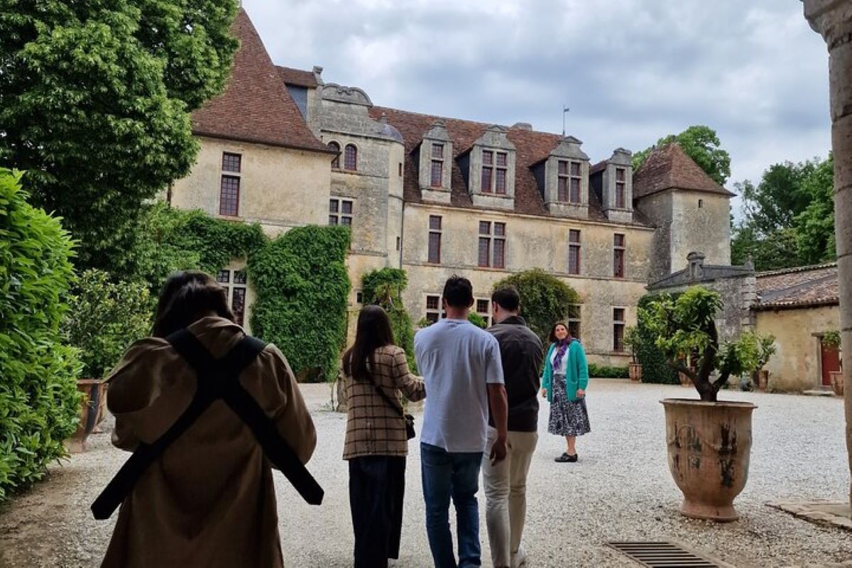 Visitors exploring a historic building surrounded by greenery, featuring a courtyard and stone architecture.