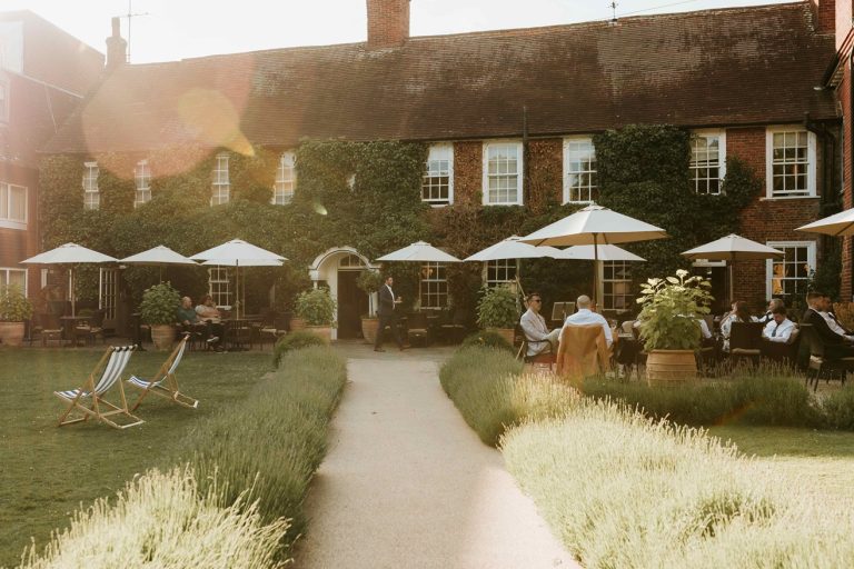 Guests enjoy outdoor seating at The Bush Farnham, surrounded by greenery and patio umbrellas on a sunny day.