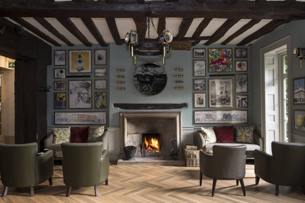 Cozy lounge area with a fireplace, elegant seating, and a gallery of framed art on the walls at The Bush Farnham Inn.