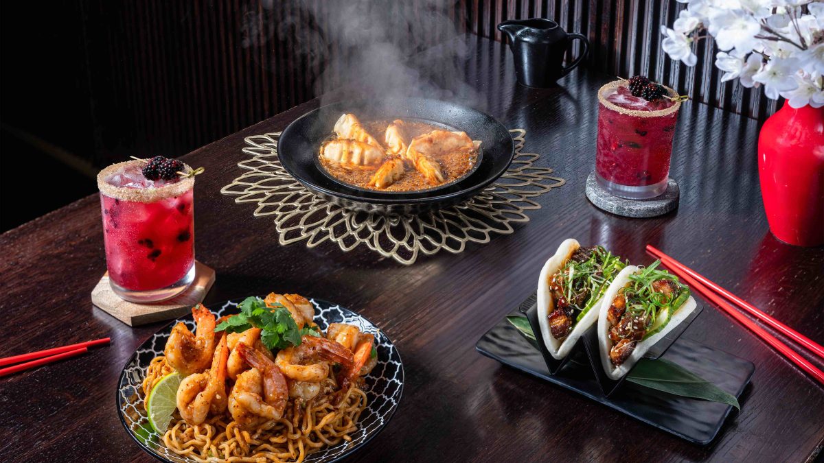 Festive table setting featuring shrimp noodles, steamed dumplings, bao buns, and colorful cocktails for Lunar New Year celebration.