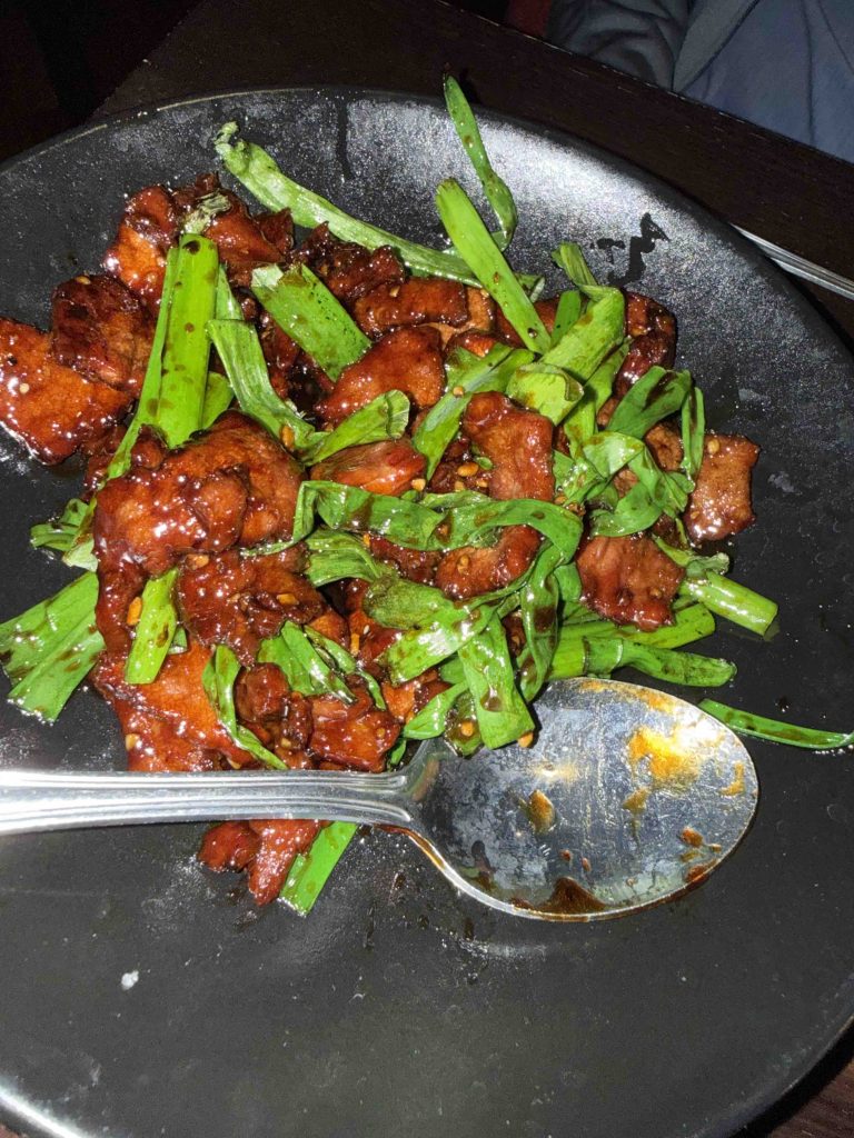Tender beef pieces glazed with a savory sauce, garnished with fresh scallions on a black plate.