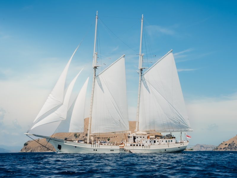 Luxury sailing yacht Mutiara Laut navigating the waters near Indonesia's hidden islands under bright blue skies.