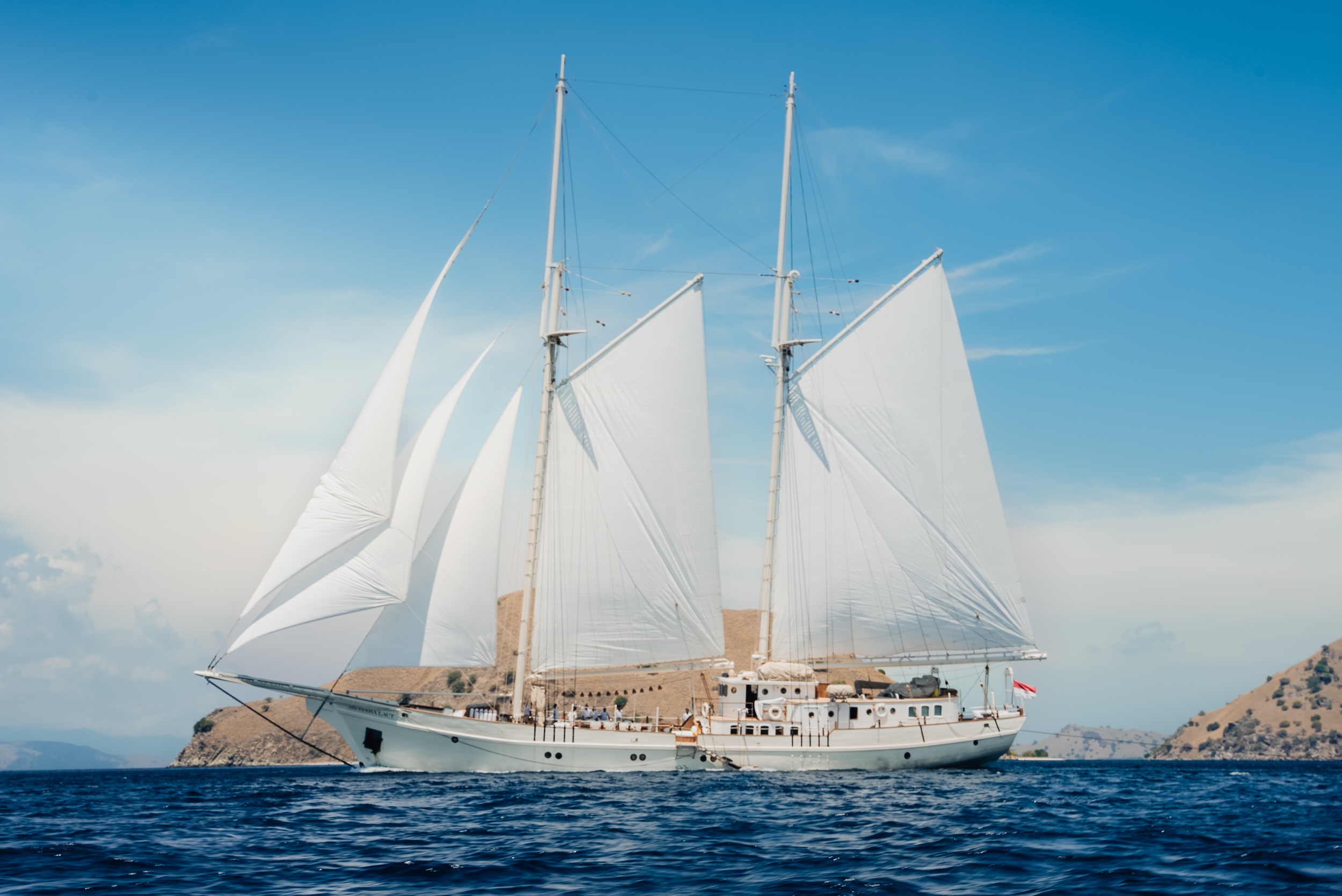 Luxury sailing yacht Mutiara Laut navigating the waters near Indonesia's hidden islands under bright blue skies.