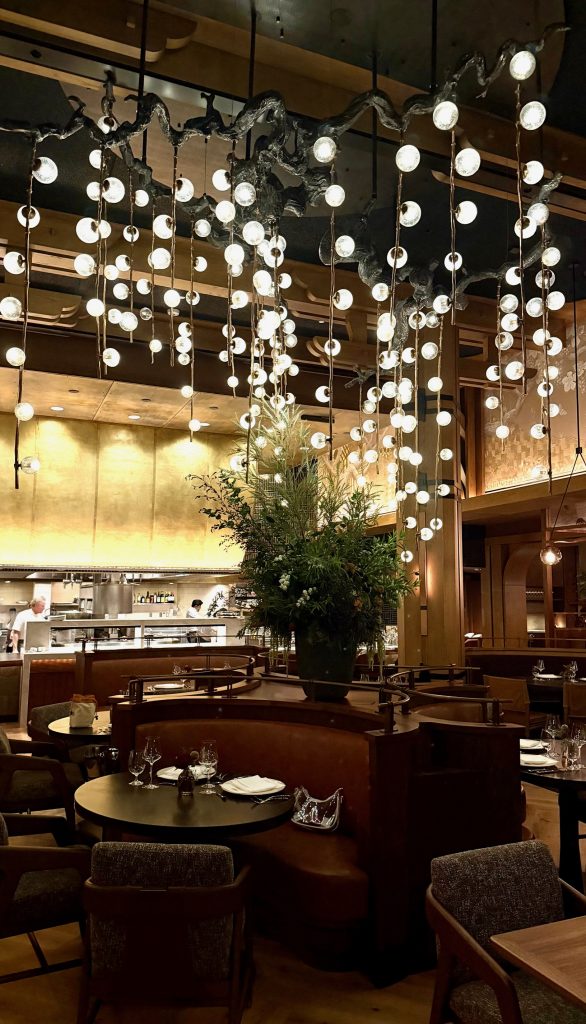 Luxurious dining area in Napa Rose featuring elegant lighting, greenery, and plush seating arrangements.