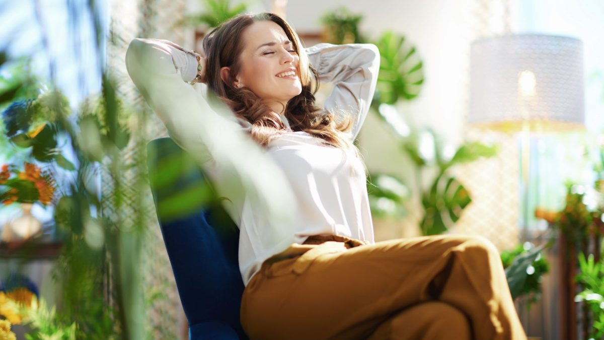Woman relaxing in a chair surrounded by indoor plants, embodying a sense of wellness and luxury in a bright living space.