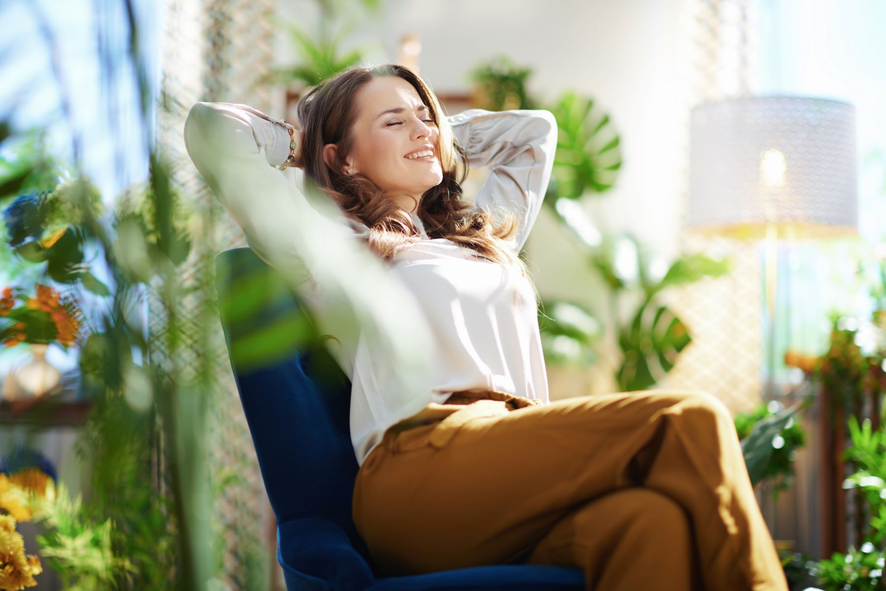 Woman relaxing in a chair surrounded by indoor plants, embodying a sense of wellness and luxury in a bright living space.