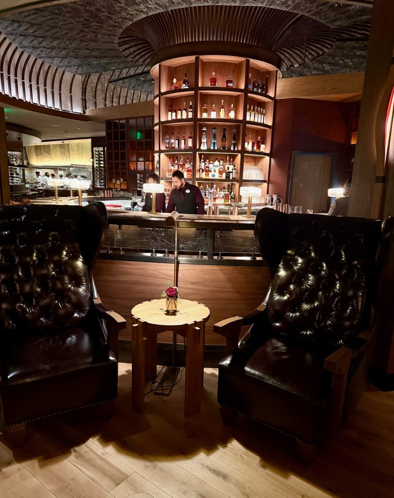 Luxurious leather chairs flanking a small wooden table with a flower vase, set against an elegant bar background.