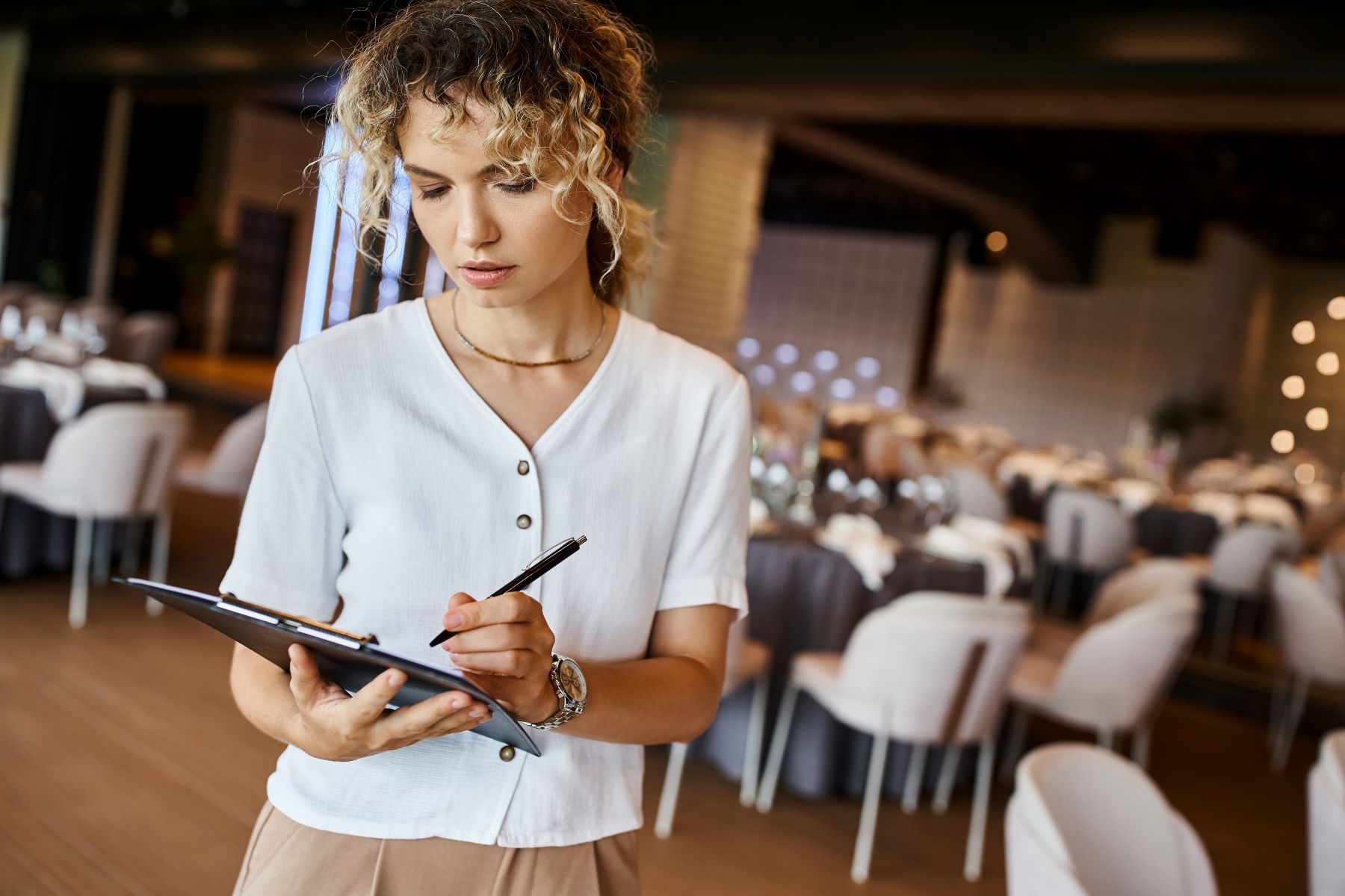 A wedding planner takes notes on a clipboard in a beautifully arranged event space.