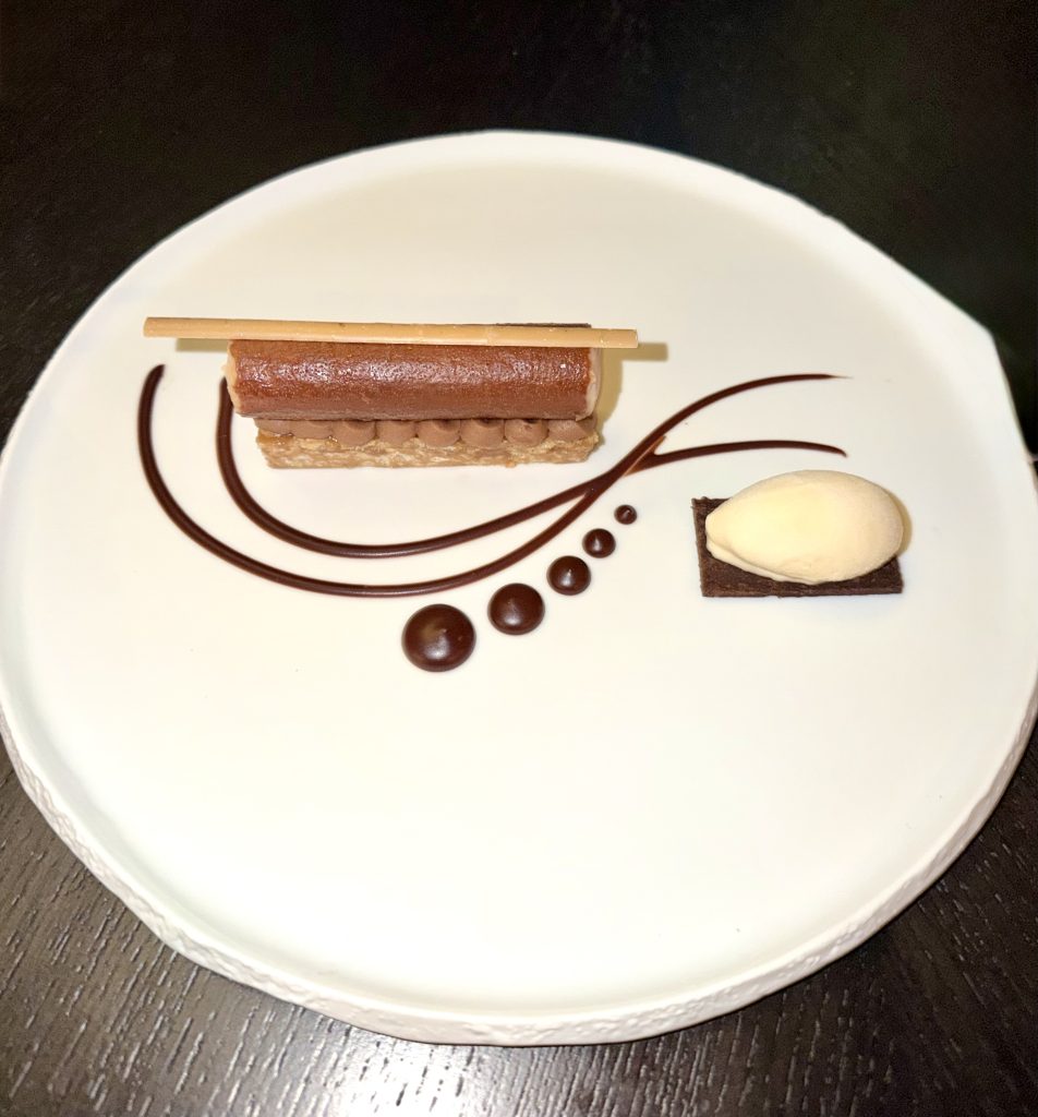 Decadent chocolate dessert plated with elegant chocolate sauce and a scoop of vanilla ice cream on a white dish.