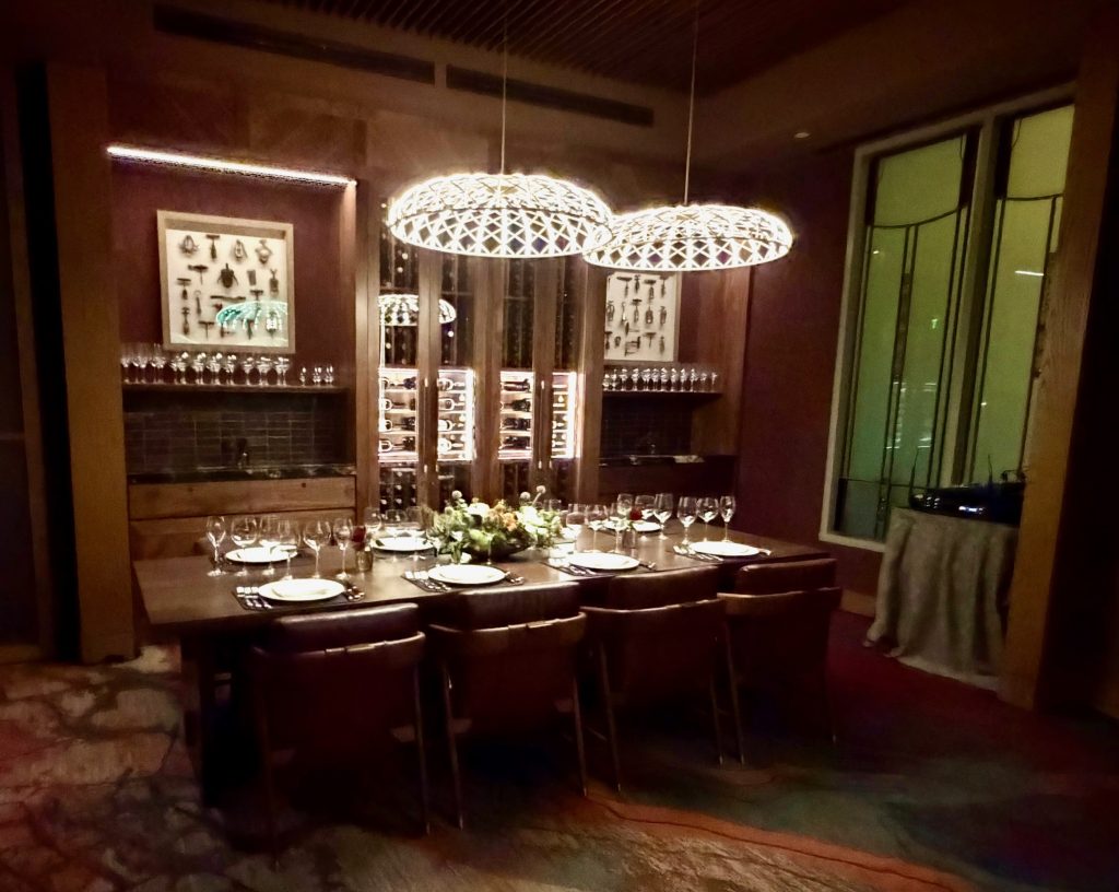 Elegant dining table set for a fine meal, surrounded by modern decor and wine storage, in a luxurious restaurant setting.
