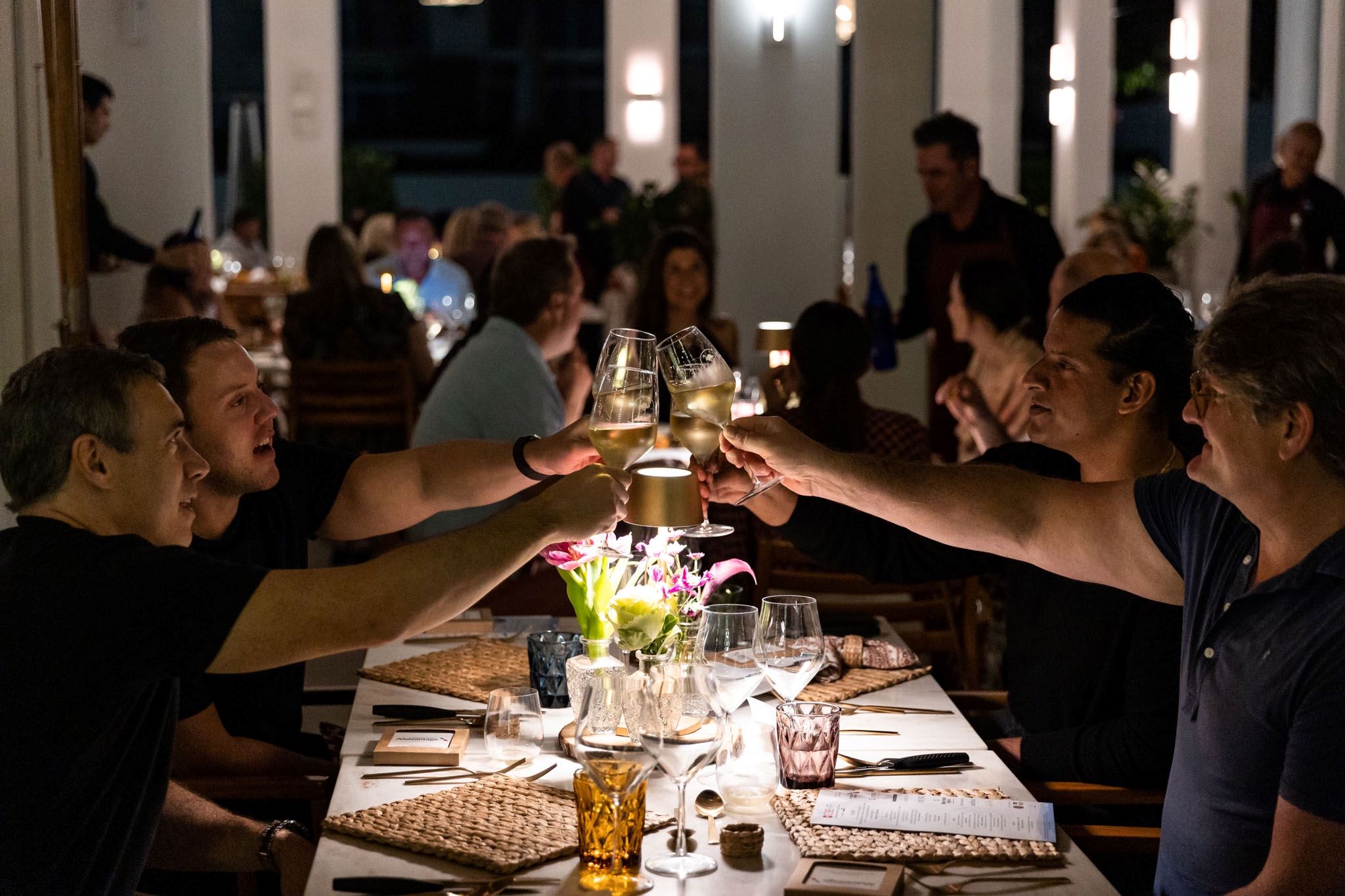 Friends celebrate with champagne glasses at a festive dinner table, surrounded by a vibrant atmosphere and soft lighting.