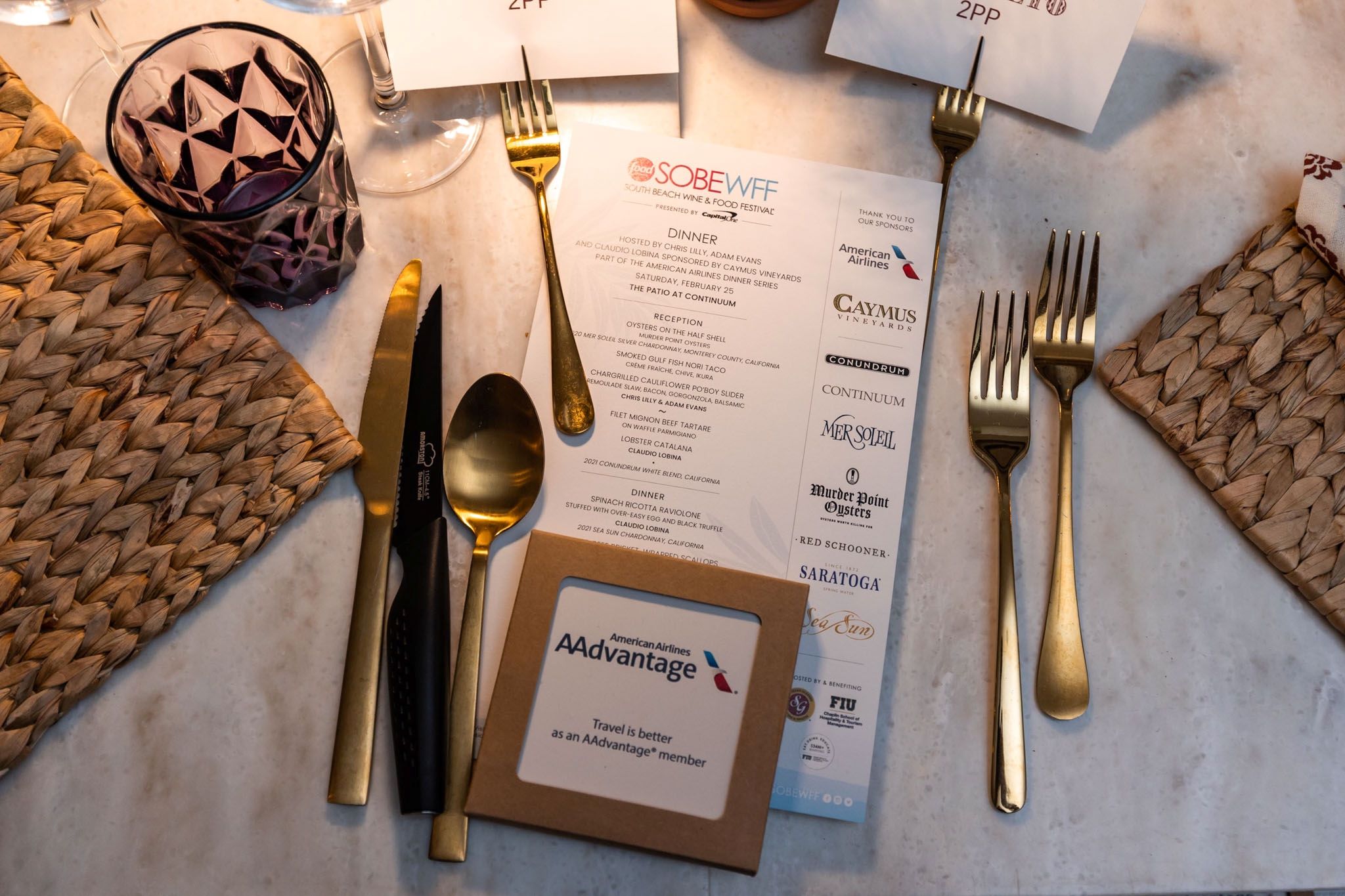 Table setting featuring gold utensils, a menu for the South Beach Wine & Food Festival, and an American Airlines AAdvantage box.