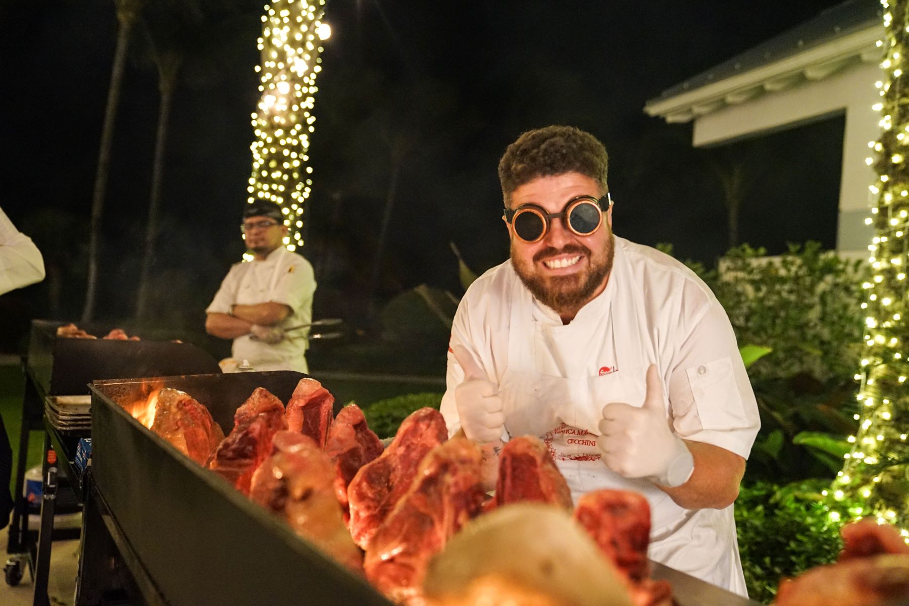 Dario Cecchini poses with thumbs up next to a grill filled with meats at the South Beach Wine & Food Festival.