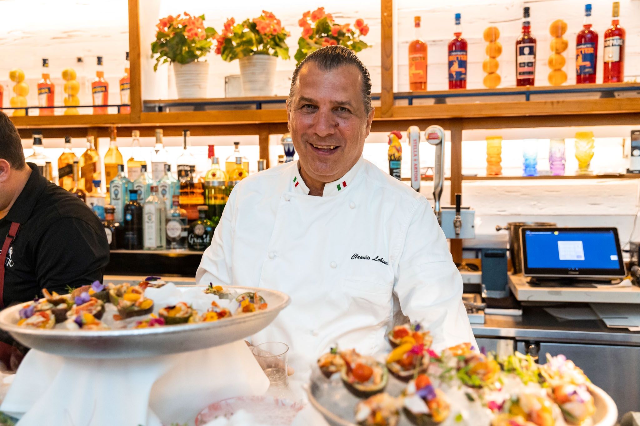 Chef Claudio Lobina smiles while presenting colorful dishes at a bar, showcasing his culinary creations during the festival.