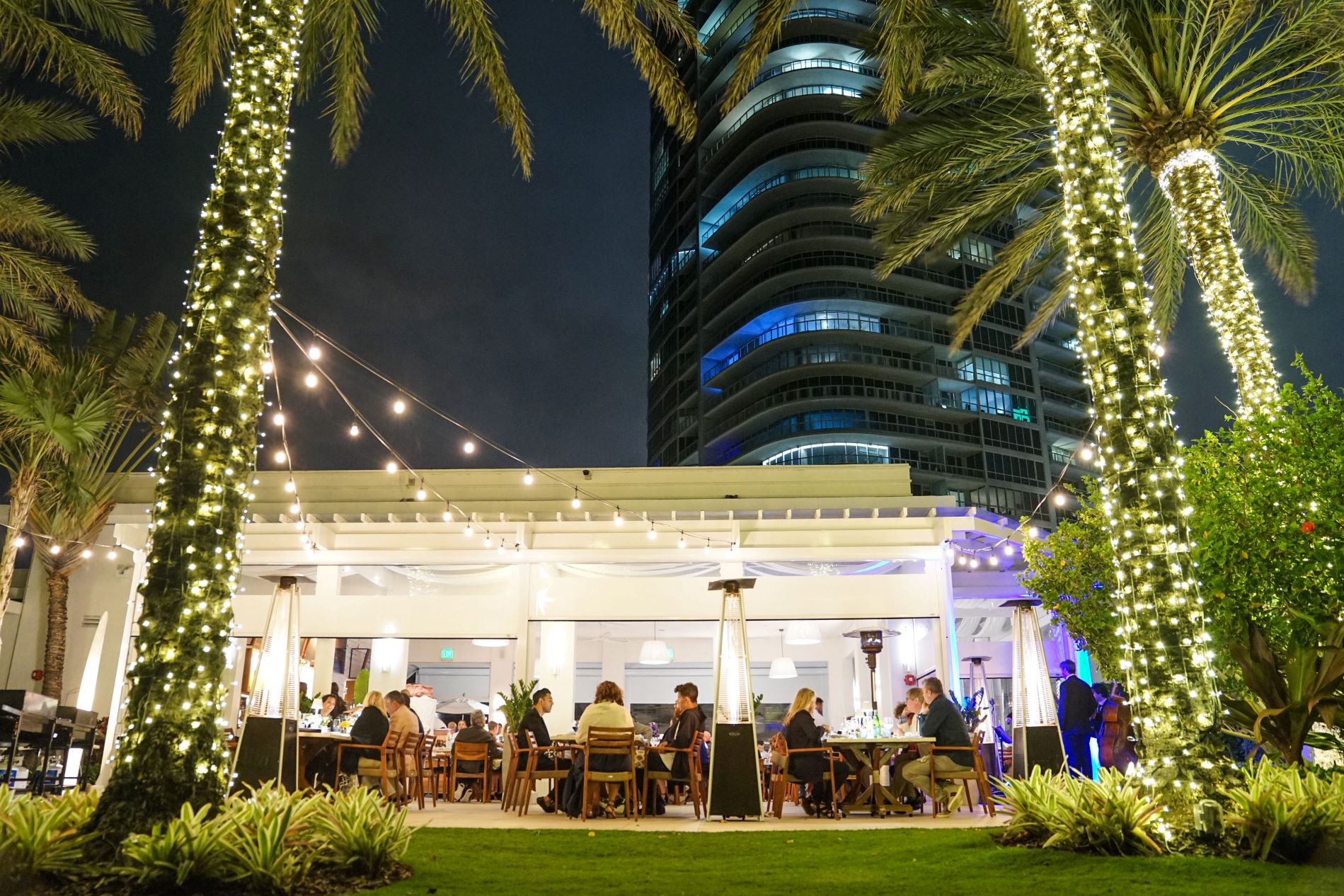The patio at Continuum features diners surrounded by palm trees and string lights near a modern high-rise in South Beach.