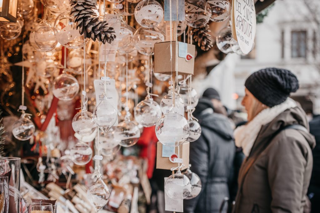 A bustling Christmas market stall adorned with ornaments and handmade goods, with visitors browsing in winter attire.