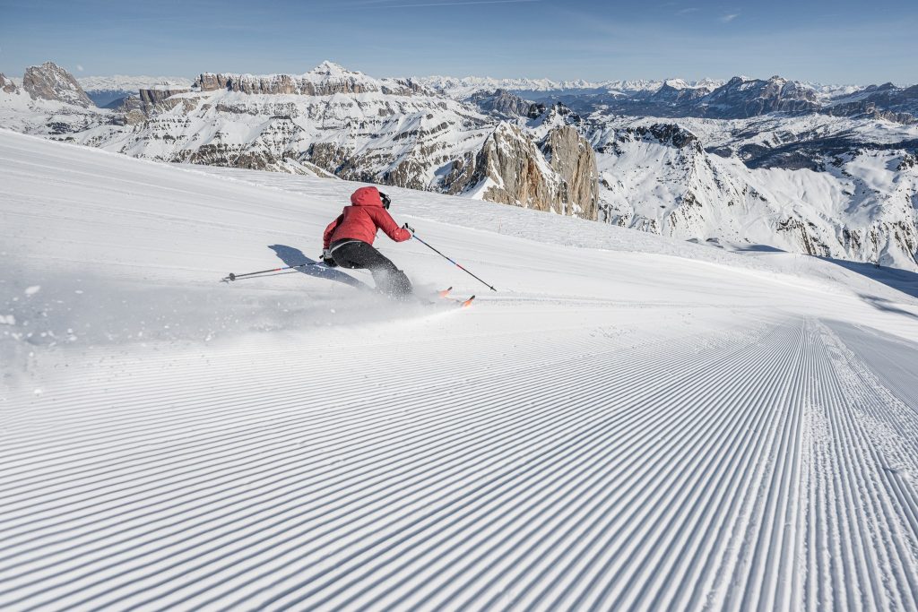 Skier in a red jacket navigating freshly groomed slopes amidst the stunning Dolomites mountain range.