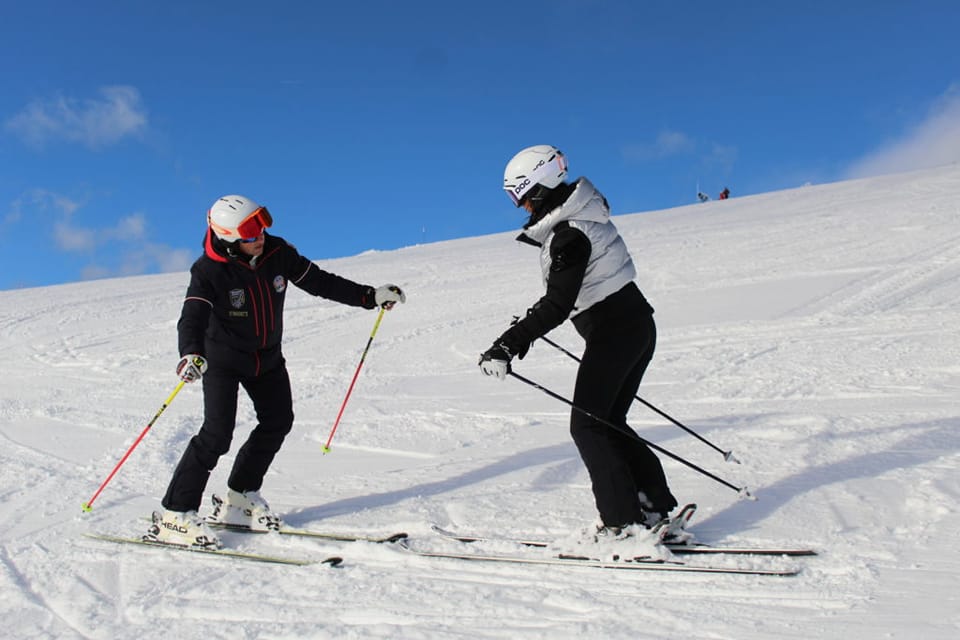 Two skiers practice on a snowy slope in the Dolomites under a clear blue sky.