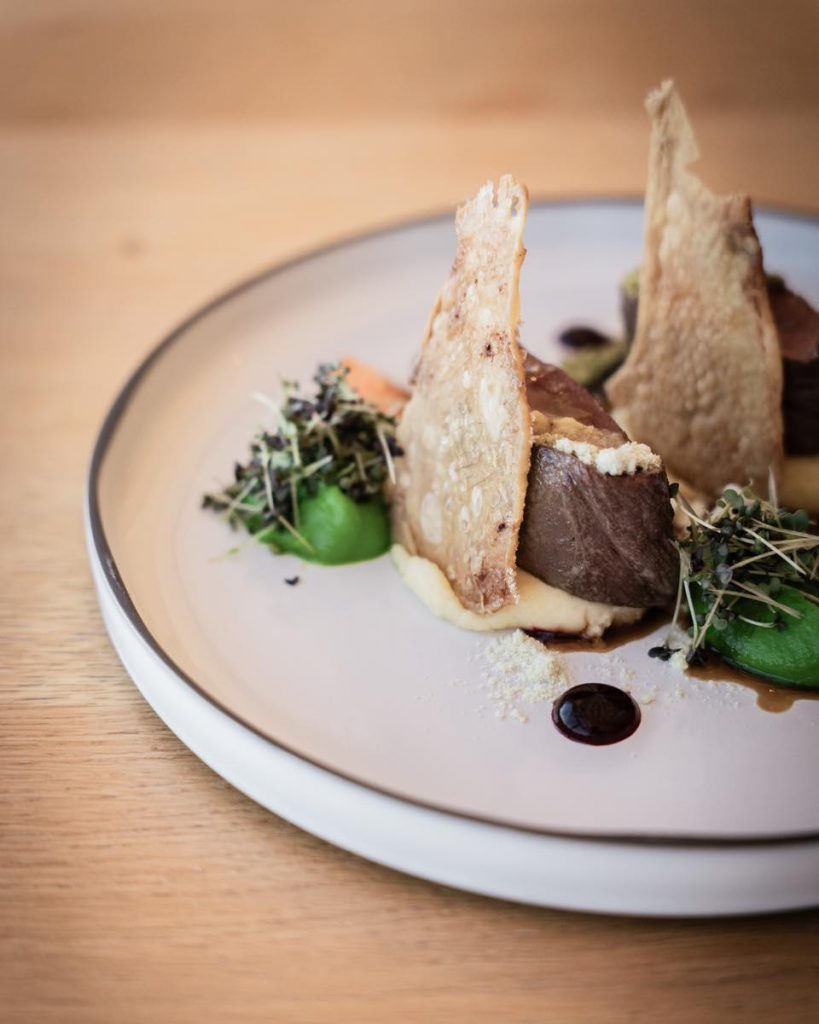 Gourmet dish featuring tender meat, crisp elements, and vibrant green accents on a modern plate.