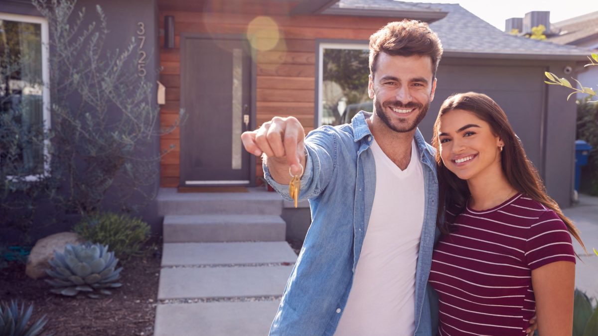 Couple happily holding keys in front of their new home, symbolizing budget-friendly first home buying experience.