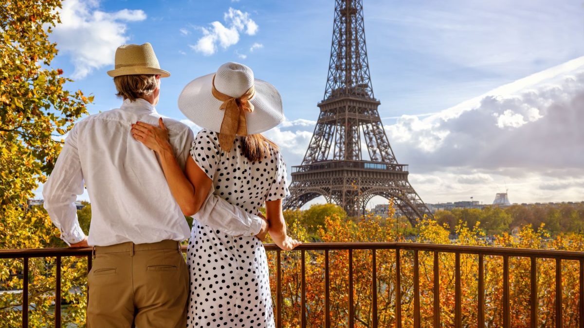 Couple enjoying a scenic view of the Eiffel Tower surrounded by autumn foliage in Paris.