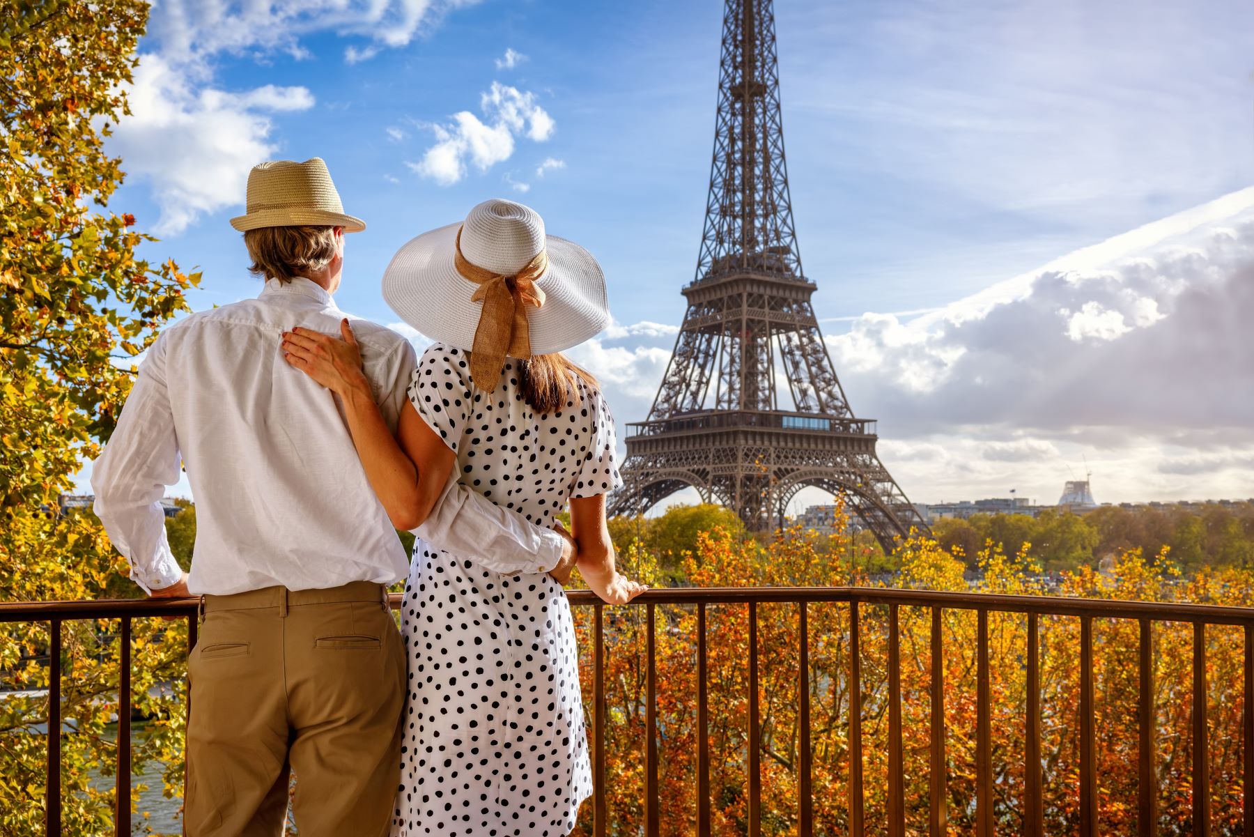 Couple enjoying a scenic view of the Eiffel Tower surrounded by autumn foliage in Paris.