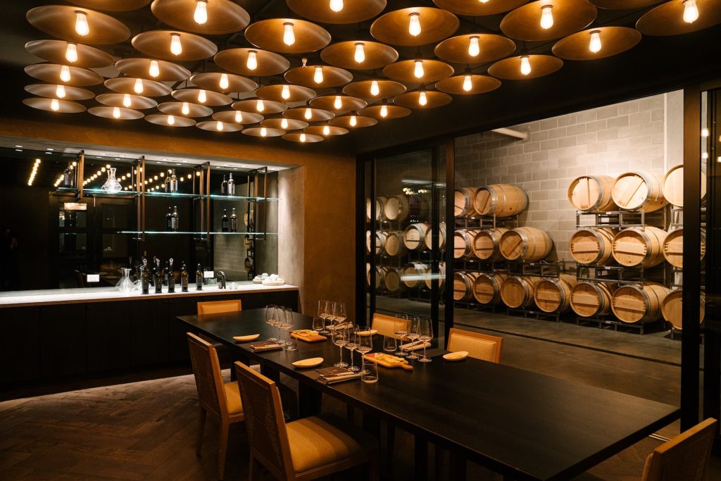 Tastefully designed dining area at Elusa Winery with glassware on the table and barrels in the background.
