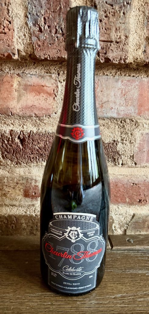 Luxury kosher champagne bottle with a black label featuring "Cheurlin Thomas" on a rustic backdrop.