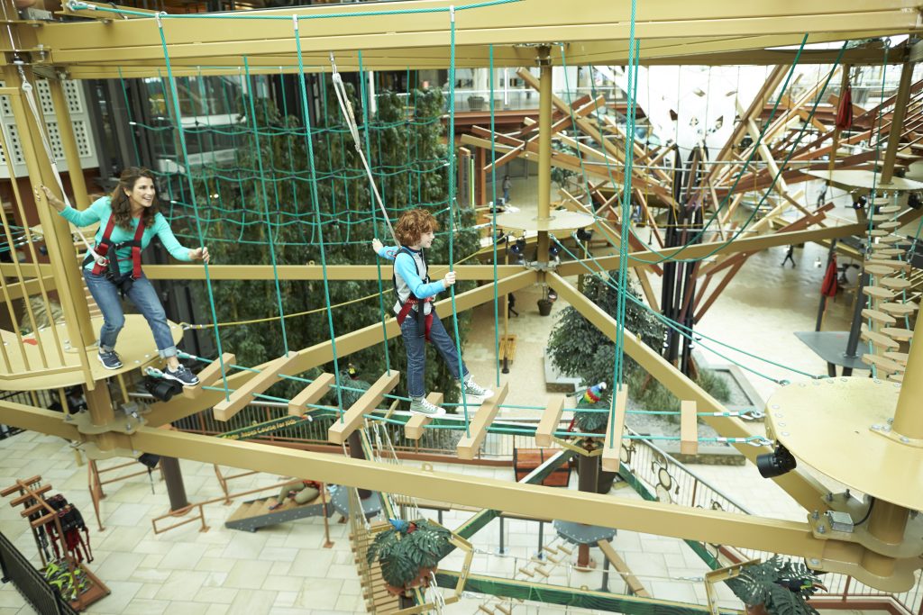 Two children navigate a ropes course at WonderWorks during Science Week, surrounded by climbing structures and greenery.