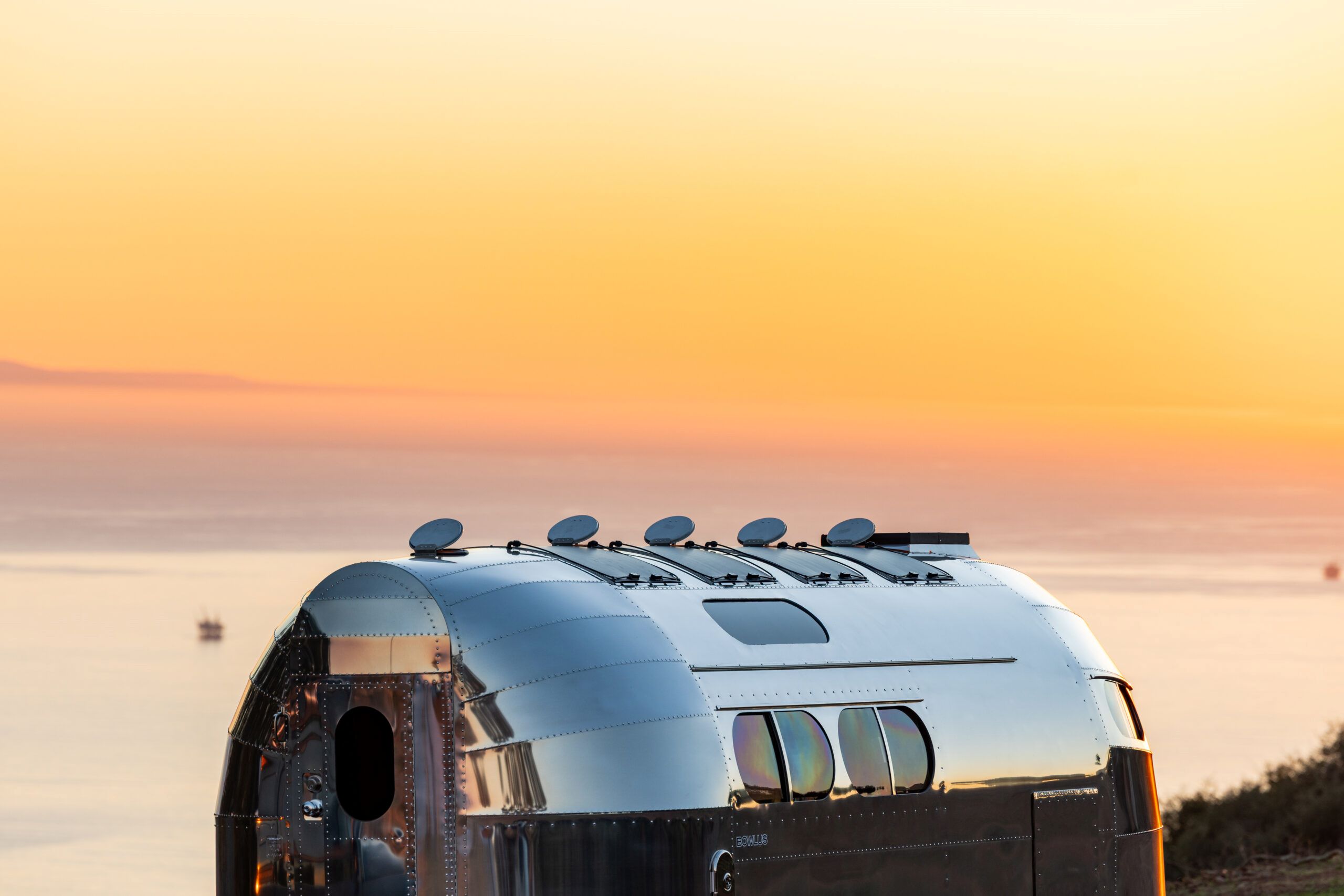 A sleek, silver RV roof with solar panels against a vibrant sunset over the ocean.
