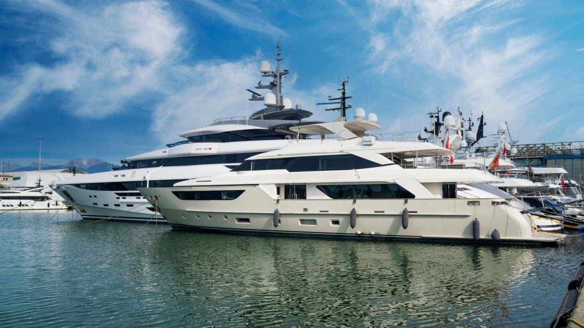 Luxury yachts docked in a marina under a blue sky, reflecting on the calm water, illustrating yacht ownership.
