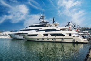 Luxury yachts docked in a marina under a blue sky, reflecting on the calm water, illustrating yacht ownership.