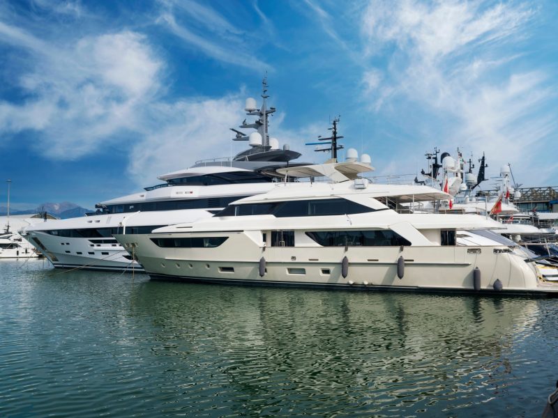Luxury yachts docked in a marina under a blue sky, reflecting on the calm water, illustrating yacht ownership.