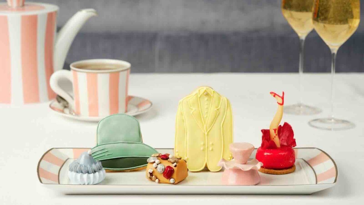 Colorful pastries resembling fashion items are displayed on a tray, alongside tea and sparkling drinks in an elegant setting.