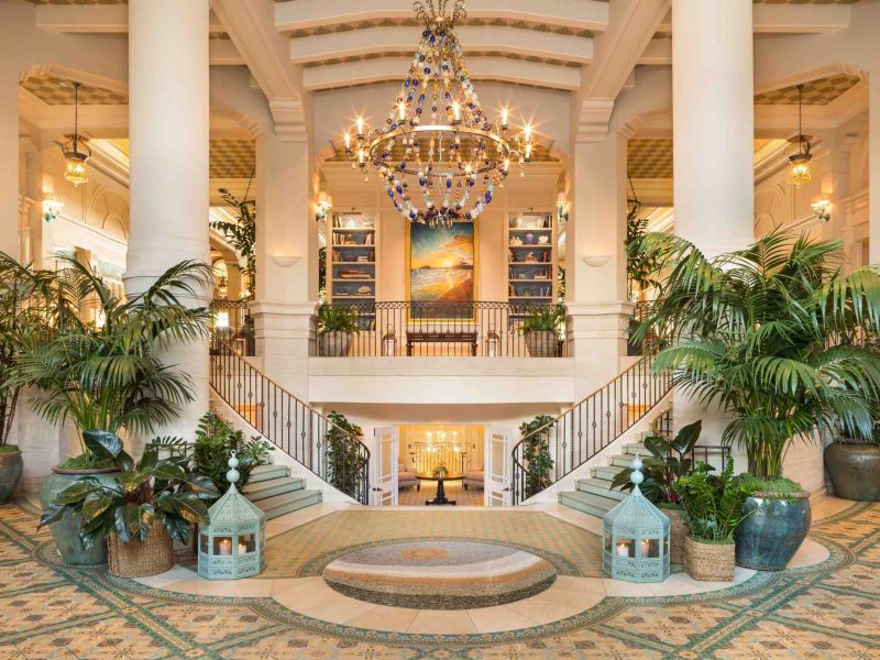Luxurious lobby of Hotel Casa del Mar features a grand chandelier, vibrant plants, and elegant staircase in a coastal setting.