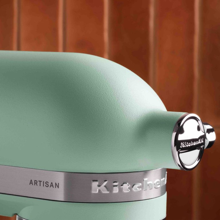 Close-up of a mint green KitchenAid mixer highlighting its sleek design and polished logo.